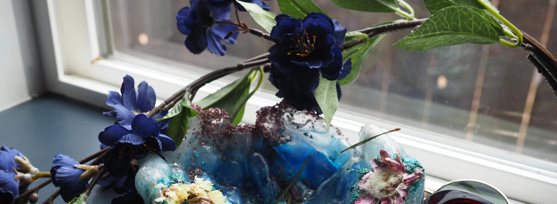 Blue sculptural material study framed by deep-blue flowers and green leaves